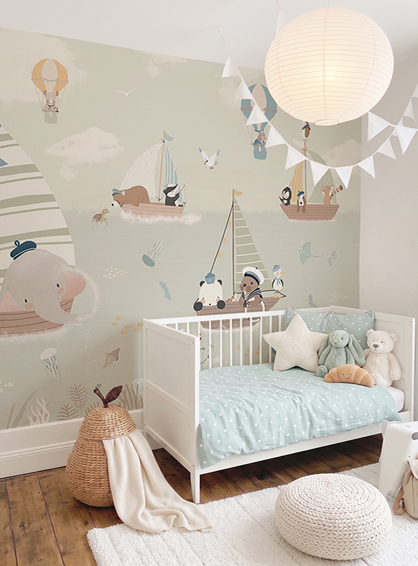 Custom made-to-measure nursery mural wallpaper called Sailing, featuring cute animals on sailboats and hot air balloons in soft sage green, dusty pink and warm beige tones, installed in a neutral whimsical nursery